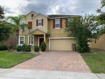 Two story home with tan exterior, red shutters, brick driveway, and two-car garage at 3742 Maidencain St, Clermont, FL 34714