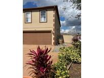 Two-story home exterior shows tan stucco, brown trim, two-car garage, and decorative landscaping at 350 Corsica Ct, Kissimmee, FL 34758