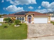 Charming single-story home with a well-manicured lawn, brick driveway, and solar panels on the roof at 5113 Sage Way, Kissimmee, FL 34758