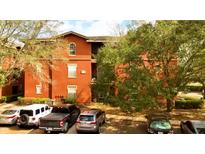 Exterior view of a red apartment building featuring mature trees and ample parking at 107 Vista Verdi Cir # 129, Lake Mary, FL 32746