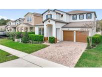 Two-story home featuring a paver driveway, two-car garage, manicured lawn, and colorful landscaping at 6974 Trellis Vine Loop, Windermere, FL 34786