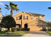 Two-story home with a tan stucco exterior, well-maintained lawn, paver driveway, and tropical landscaping at 2677 San Simeon Way, Kissimmee, FL 34741