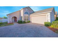 Charming single-story home with a brick driveway, arched entry, well-maintained landscaping, and attached two-car garage at 153 Cambridge Ave, Davenport, FL 33896