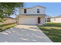 Two-story home featuring attached garage, driveway, landscaped yard, and a red front door at 49 Inconnu Dr, Poinciana, FL 34759