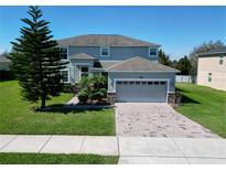 Two-story home featuring a well-manicured front lawn, paver driveway, and neutral-toned exterior with stone accents at 1336 Lattimore Dr, Clermont, FL 34711