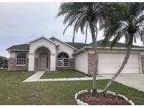 Charming single-story home featuring a well-manicured lawn, brick accents, and mature palm trees at 2438 Winfield Dr, Kissimmee, FL 34743