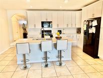 Bright kitchen boasts white cabinetry, modern appliances, island with seating, and tiled floors at 3082 Royal Tern Dr, Winter Haven, FL 33881