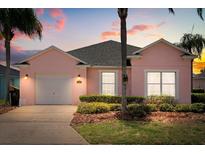 Charming pink single-story home featuring lush landscaping and a well-maintained front yard at dusk at 407 Reserve Dr, Davenport, FL 33896
