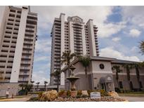 Exterior view of a multi-story building with a fountain and landscaping in front under a cloudy sky at 13427 Blue Heron Beach Dr # 1607, Orlando, FL 32821