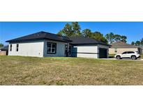 Lovely single-story home with neutral stucco, a dark roof, a dark two-car garage, and well-manicured yard at 4491 Sw 151 St, Ocala, FL 34473
