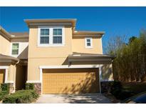 Two story tan home featuring a two car garage, manicured landscaping, and a stone facade on the bottom of the house at 17459 Chateau Pine Way, Clermont, FL 34711