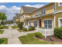 Charming yellow townhomes with red doors and white picket fences line a sidewalk on a sunny day at 2604 Lodi Cir # 103, Kissimmee, FL 34746