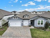 Beautiful, gray single-story home with a three-car garage and brick-paved driveway on a sunny day at 2768 Matera Dr, St Cloud, FL 34771