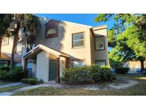 Tan two-story townhome featuring a quaint front porch and lush landscaping at 5436 E Michigan St # 5, Orlando, FL 32812