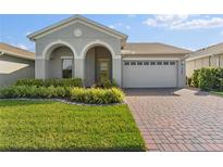 Charming home featuring manicured lawn, brick driveway, and welcoming arched entryway at 7465 Wing Span Way, Harmony, FL 34773