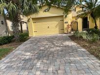 Paver driveway leads to a yellow two-car garage and gated courtyard at 2502 Palm Tree Dr, Poinciana, FL 34759