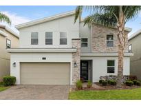 Modern two-story home boasts a neutral color scheme, stone accents, manicured landscaping, and a brick paver driveway at 581 Pebble Beach Dr, Davenport, FL 33896