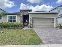 Inviting front exterior with stone accents, well-maintained lawn, brick driveway, and attached two-car garage at 195 Preston Ave, Davenport, FL 33837