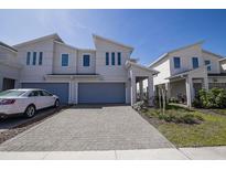 Modern townhome featuring a gray two-car garage, brick driveway, and manicured landscaping at 3470 Beau Rd, Kissimmee, FL 34746