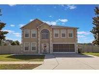 Two-story home with tan stucco exterior, arch window detail, attached two-car garage, and well-manicured lawn at 7716 Park Hill Ave, Leesburg, FL 34748