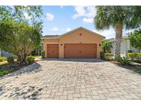 Charming single-story home featuring a three-car garage and a brick-paved driveway, plus lush landscaping at 1825 Pelican Hill Way, Kissimmee, FL 34759