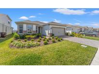 Well-manicured front yard and neutral-colored home with a two car garage under a sunny blue sky at 2019 Spring Shower Cir, Kissimmee, FL 34744