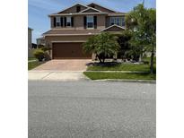 Inviting two-story home with a brick driveway, lush landscaping, and a welcoming front porch at 2528 Needlepoint St, Kissimmee, FL 34741