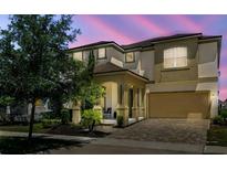 Inviting two-story home with a covered front porch, two-car garage, and paver driveway at dusk at 1817 Caribbean View Ter, Kissimmee, FL 34747