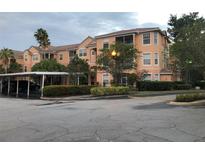 Three-story building with colorful, light-orange walls, a landscaped garden, and a carport at 13500 Turtle Marsh Loop # 825, Orlando, FL 32837