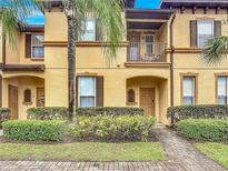 Townhome exterior with yellow stucco, a palm tree, a brick walkway, and shutters at 247 Verona Ave, Davenport, FL 33897