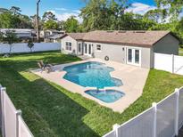 A backyard pool and spa, surrounded by a concrete deck, a well-maintained lawn, and a white fence at 7823 Bell Blvd, Orlando, FL 32810