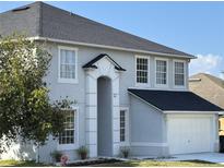Two-story home featuring light gray stucco, white trim, and a black roof under a clear blue sky at 1976 The Oaks Blvd, Kissimmee, FL 34746