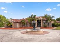 Stately brick home featuring a circular driveway, large fountain, mature landscaping, and grand entrance, with a red tile roof at 2841 S Lloyd Ln, Kissimmee, FL 34744