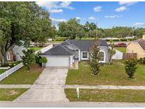 Single story home with a gray exterior, attached garage, green lawn and mature trees at 5642 Chukar Dr, Orlando, FL 32810