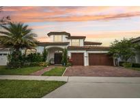 Elegant two-story home with a three-car garage, beautiful landscaping, and a brick driveway under a captivating sunset sky at 13136 Alderley Drive Dr, Orlando, FL 32832