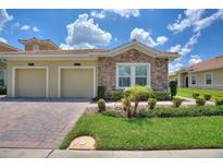 Charming villa featuring stone accents, a two-car garage, and well-maintained landscaping under a sunny, partly cloudy sky at 1082 Blackwolf Run Rd, Davenport, FL 33896