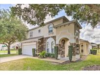 Charming two-story home featuring a well-manicured lawn and a stone-accented facade under a tree-shaded sky at 214 Tupelo Cir, Davenport, FL 33897