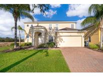 Two-story home featuring manicured lawn, palm trees, brick driveway, and a two-car garage at 389 Yellow Snapdragon Dr, Davenport, FL 33837