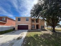 Two-story peach home with a red garage door and a well-maintained front lawn at 340 Cimarron Ct, Poinciana, FL 34759