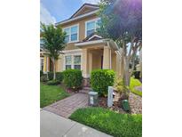Charming two-story townhome featuring lush landscaping, a brick walkway, and a welcoming covered porch at 7673 Ripplepointe Way, Windermere, FL 34786