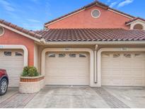 Charming condo featuring multi-car garage with neutral tone doors, orange-colored stucco, and Spanish tile roofing at 7865 Sugar View Ct # 7865, Orlando, FL 32819