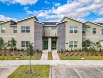 Modern townhome exterior featuring gray stone accents and vibrant green doors under a partly cloudy sky at 2970 Protagonist St, Kissimmee, FL 34746