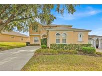 Charming two-story peach home featuring an arched entry, manicured lawn, and a lengthy driveway at 303 Plumoso Loop, Davenport, FL 33897