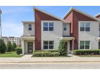 A modern townhouse with gray stucco and red siding, featuring a well-manicured lawn and inviting entrance at 185 E Warren Ave, Longwood, FL 32750