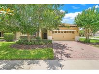 Charming single-story home with a well-manicured lawn, mature trees, and a brick-paved driveway leading to a two-car garage at 1300 Island Green St, Davenport, FL 33896
