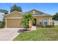 Charming single-story home featuring a well-manicured lawn, brick driveway, and a beautiful palm tree in the front yard at 15341 Groose Point Ln, Clermont, FL 34714