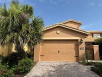 Two car garage with brick paved driveway and mature landscaping with palm tree and desert bushes at 2495 Palm Tree Dr, Kissimmee, FL 34759