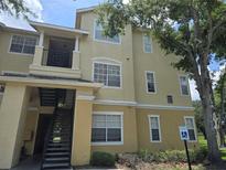 Inviting exterior view of the two-story building, featuring a staircase and a balcony under a partly cloudy blue sky at 2572 Robert Trent Jones Dr # 1227, Orlando, FL 32835