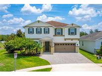 Two-story home with a brick paved driveway, two-car garage, green shutters, and manicured landscaping at 14421 Ward Rd, Orlando, FL 32824