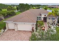 Beautiful waterfront home with brick driveway, three-car garage, tile roof, and lush tropical landscaping at 561 Tapatio Ln, Kissimmee, FL 34759
